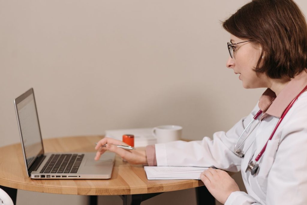 Doctor writing visit notes and updating the medical record on a laptop