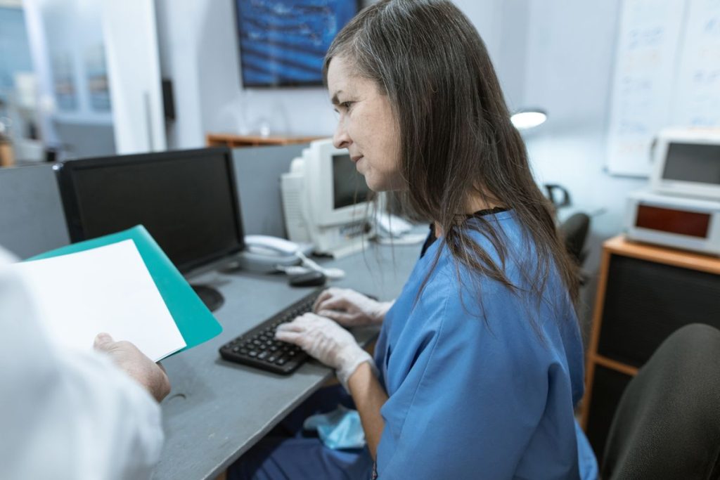 Healthcare worker typing at a medical workstation while reviewing EHR documentation